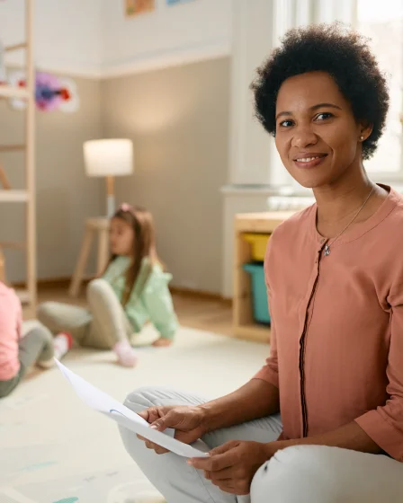 woman sitting with a child in the background in a childcare setting