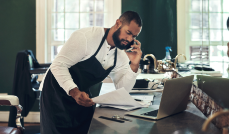 barber talking on the phone with a laptop and documents on the table used on a blog about how to make an insurance claim