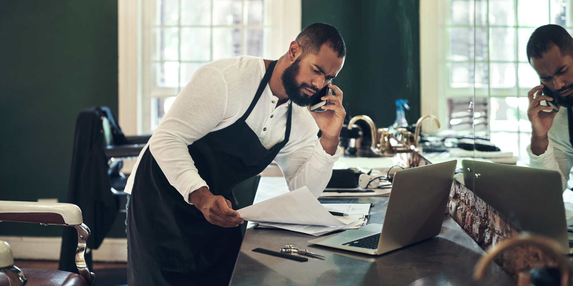 barber talking on the phone with a laptop and documents on the table used on a blog about how to make an insurance claim