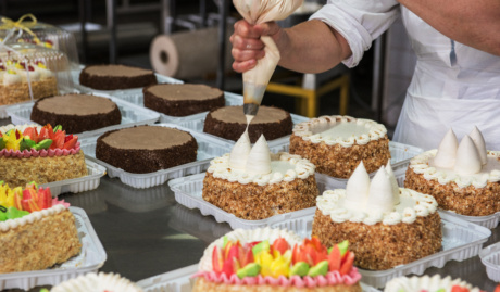 someone piping decoration on a cake in a large scale cake production setting used on a blog about product liability insurance