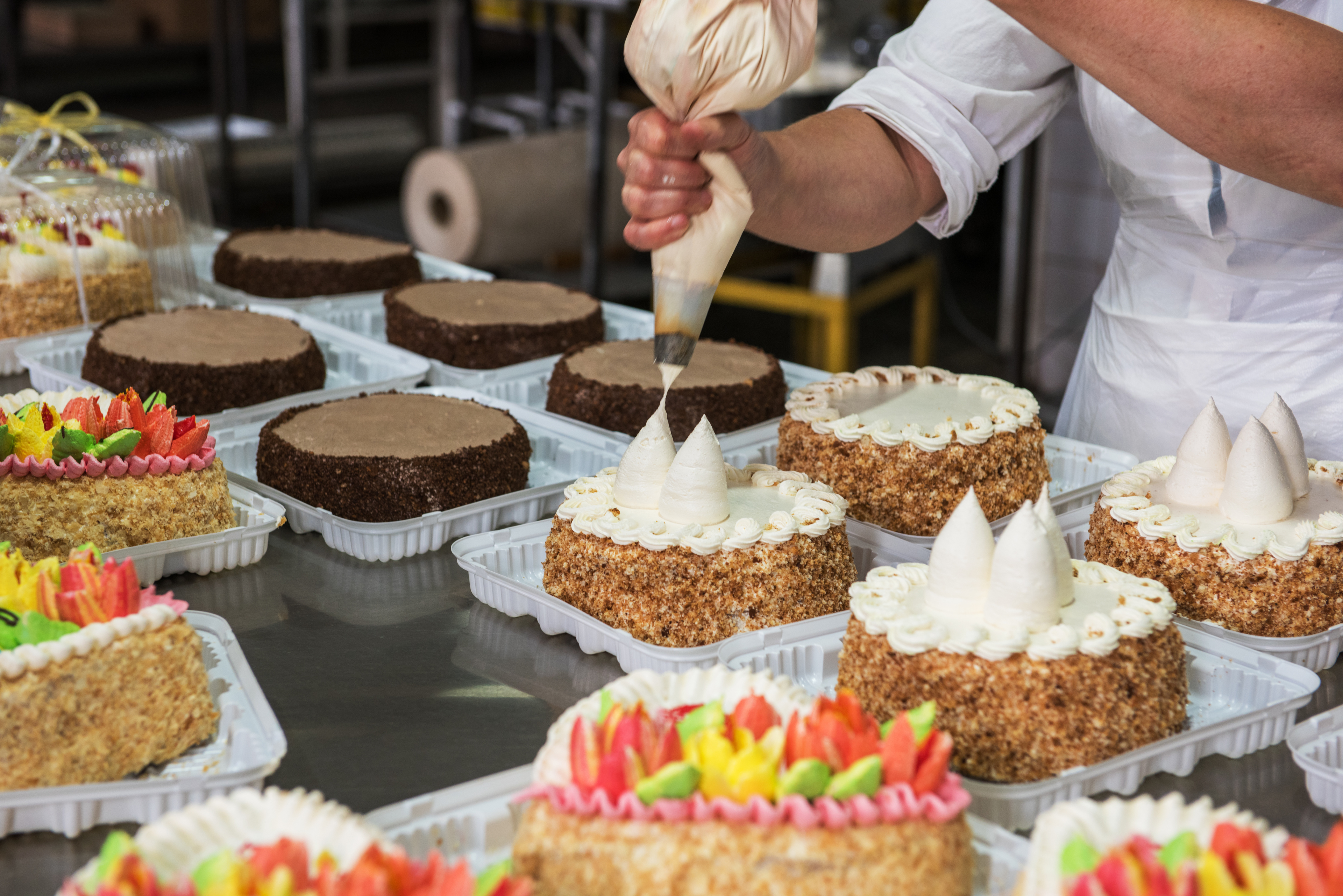 someone piping decoration on a cake in a large scale cake production setting used on a blog about product liability insurance