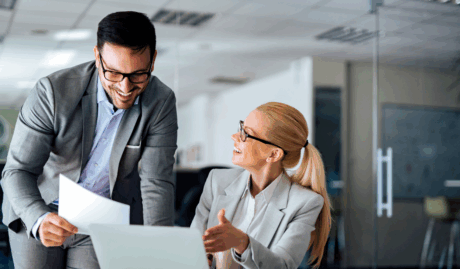 man and woman in grey suits looking at documents smiling used on a blog about professional services insurance