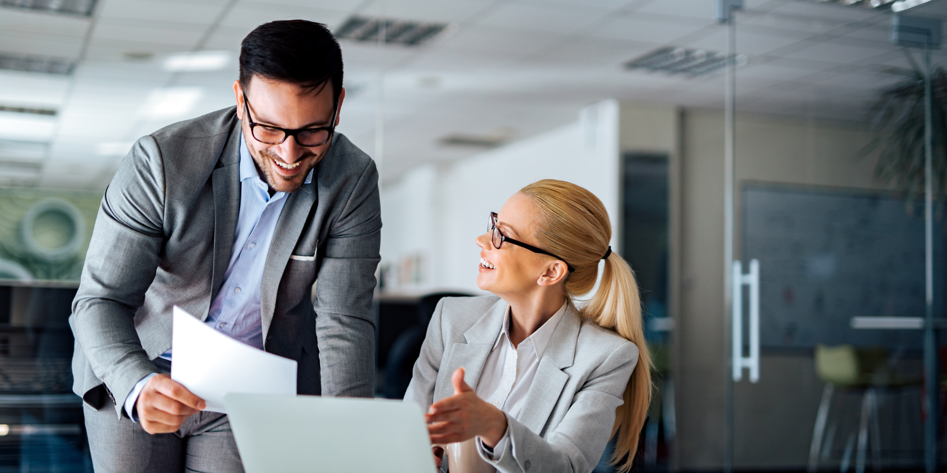 man and woman in grey suits looking at documents smiling used on a blog about professional services insurance
