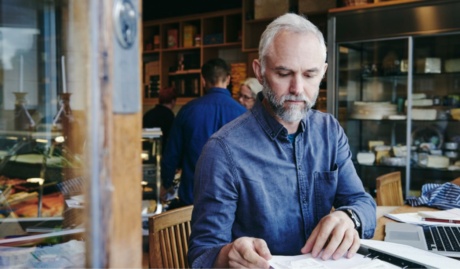 man sitting reviewing papers with an open laptop used on a blog about business insurance requirements and EOFY
